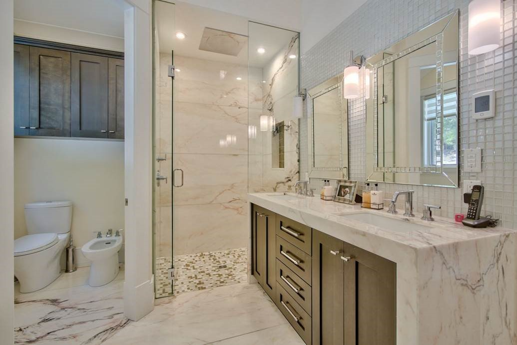 A modern bathroom features a glass shower, dual sinks, and elegant marble finishes