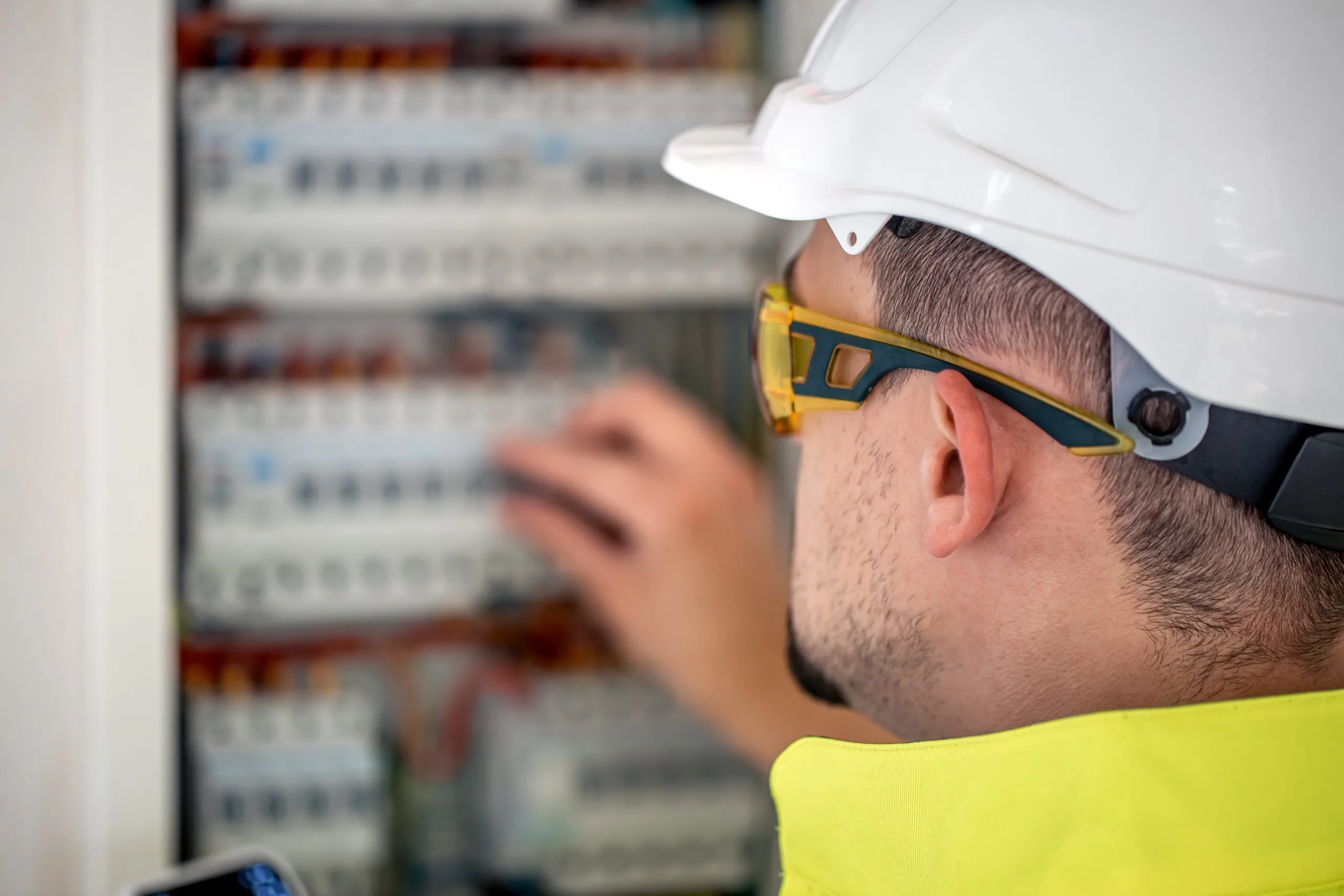 A worker in safety gear adjusts wiring in an electrical panel