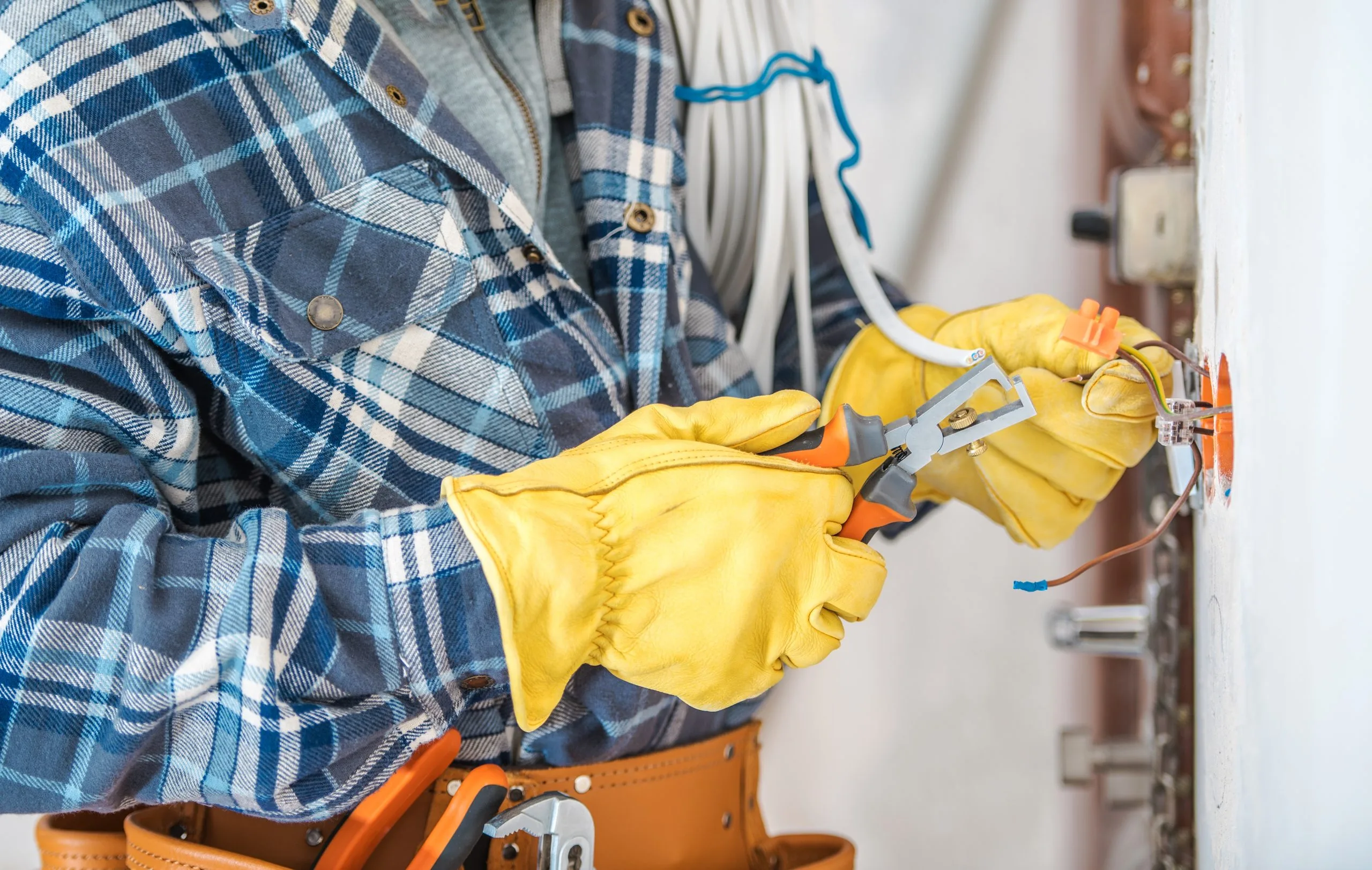 A person in a plaid shirt and yellow gloves works on electrical wiring