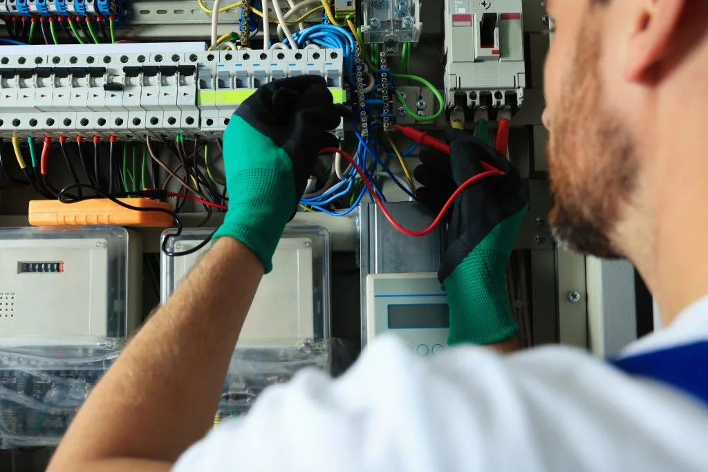 A technician in gloves works on wiring inside an electrical control panel