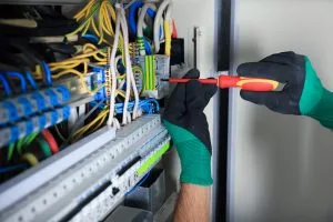 A person in gloves performs electrical work on colorful cables and equipment