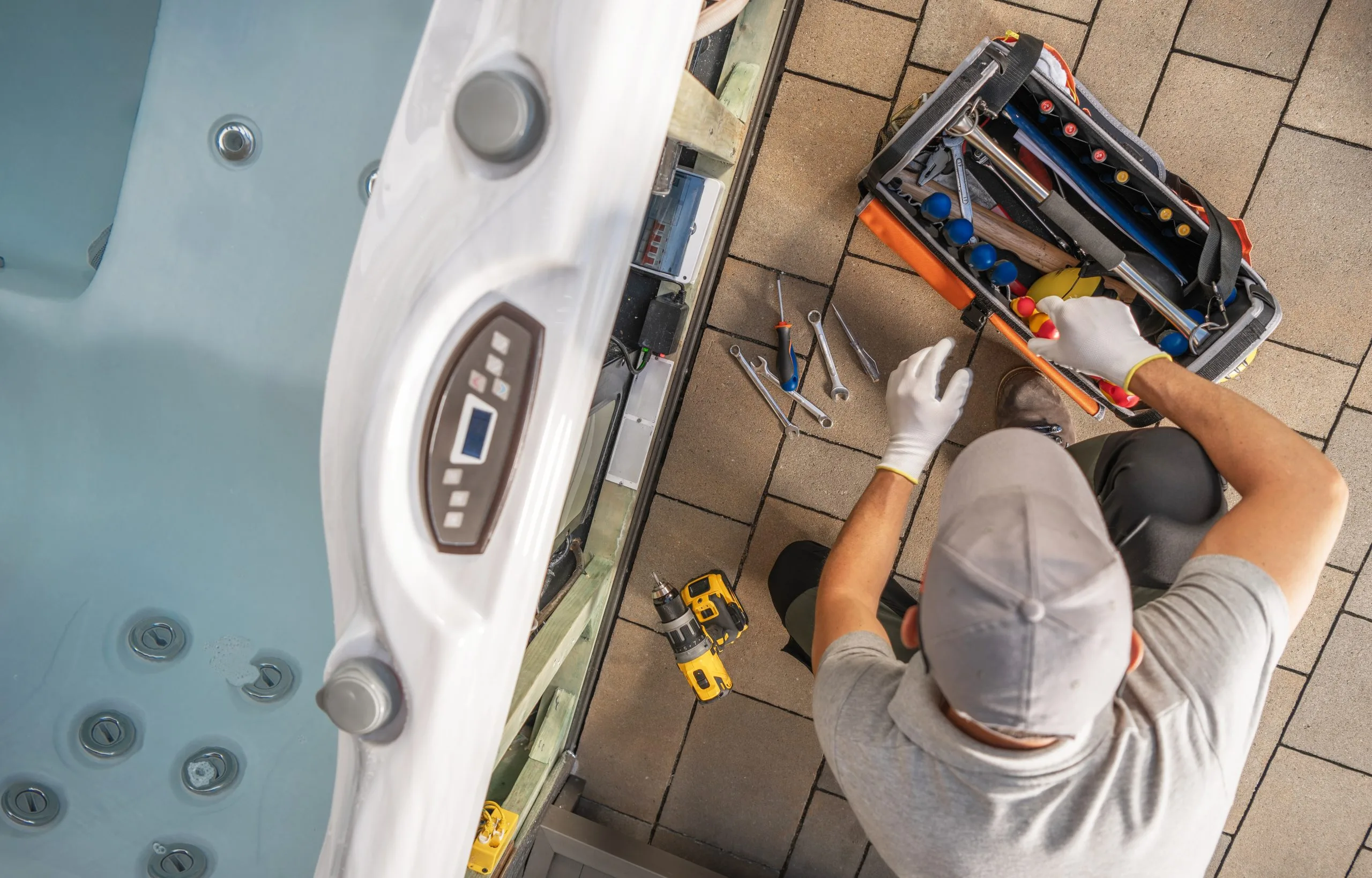 A person in a gray cap works on a tool box near a hot tub