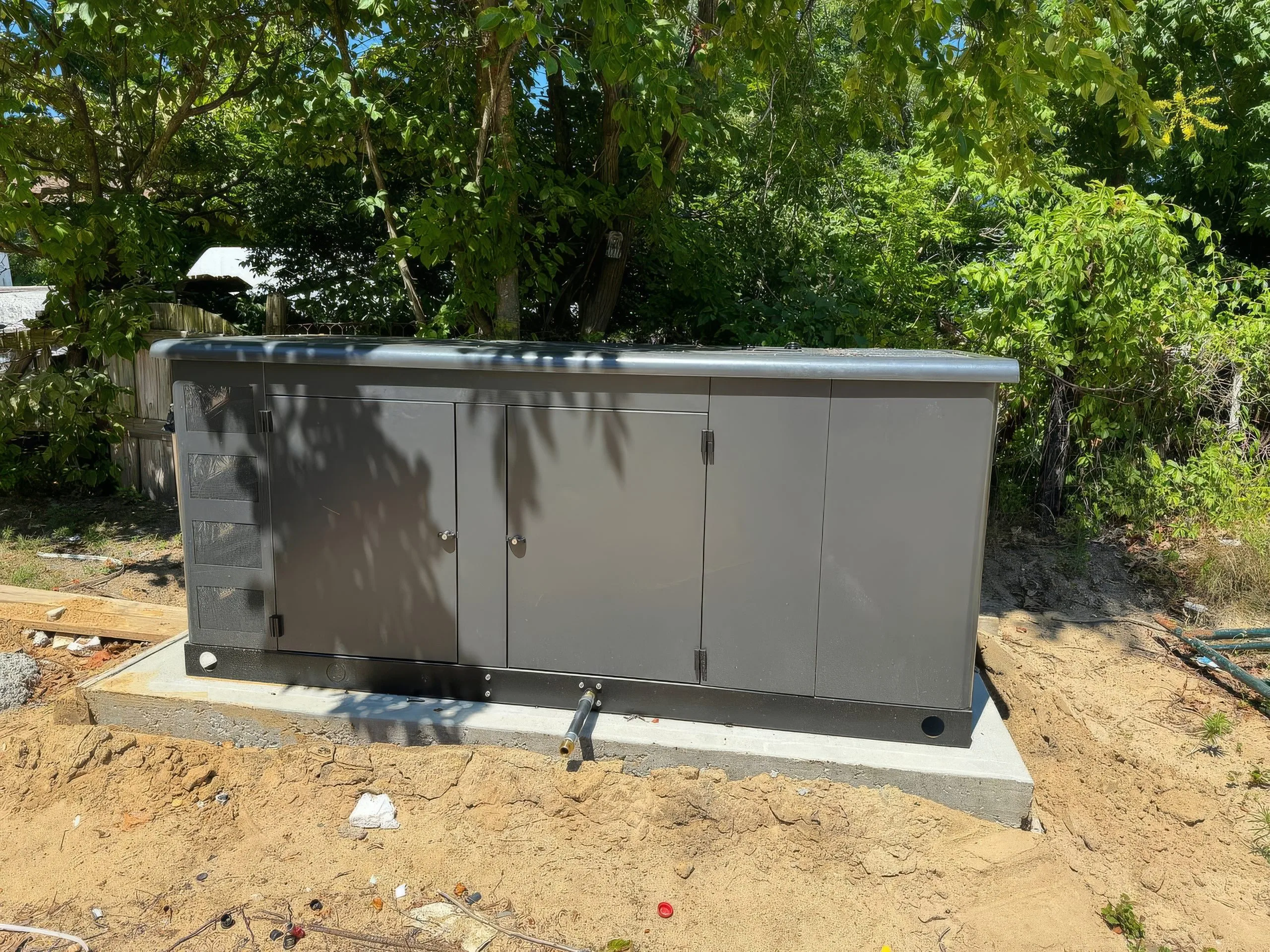 A gray utility box stands on a concrete slab surrounded by greenery