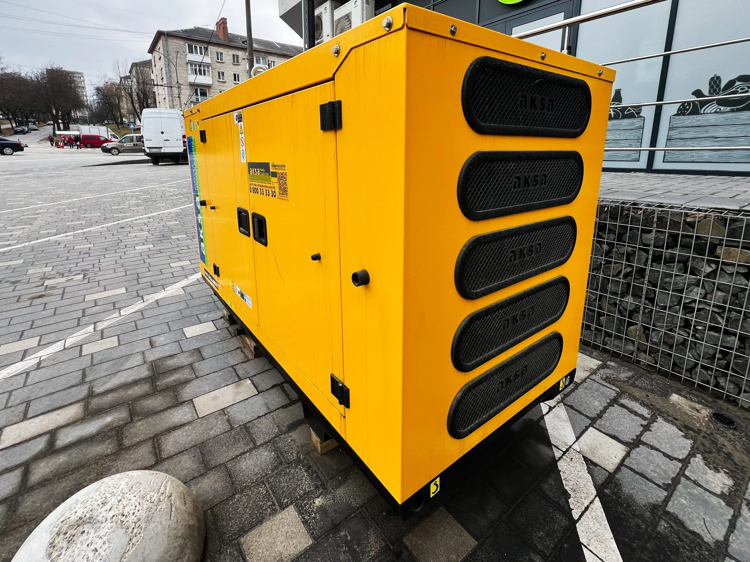 A bright yellow generator is parked on a cobblestone surface near buildings