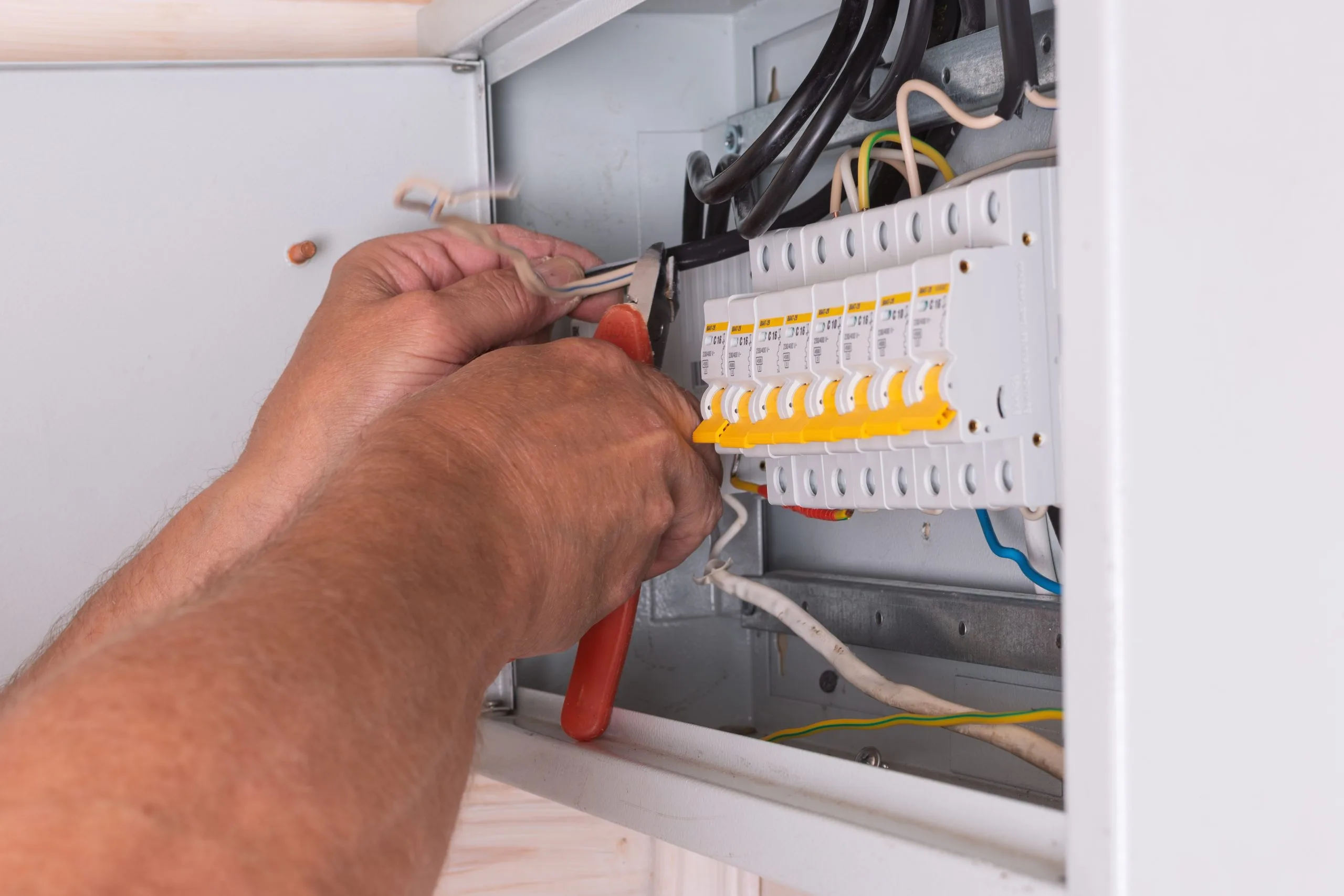 A person is working on an electrical panel, adjusting wires and connections